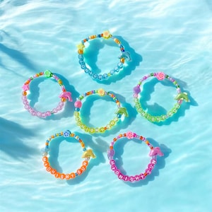 May include: Six colorful beaded bracelets with the words "MIDNIGHT SUN" spelled out in white beads. Each bracelet features a different color scheme, including pink, orange, yellow, green, and blue, with dolphin and flower charms.