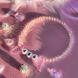 May include: A pink crystal beaded bracelet with a charm that says "444" and two pink angel wings.
