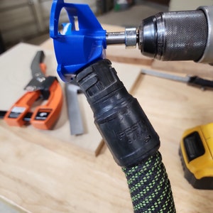 May include: A blue plastic dust collection attachment for a drill, connected to a black and green hose with a "Festool Clean" label.