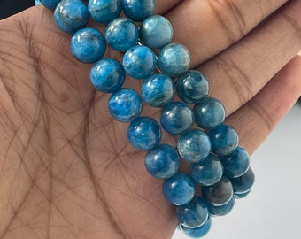 May include: A bracelet composed of multiple strands of polished, round blue apatite beads. The beads exhibit varying shades of deep and light blue with natural internal inclusions and a smooth, glossy finish, strung together in a multi-row design.