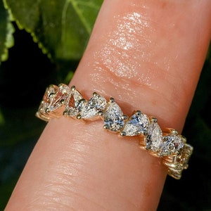 May include: A gold band ring with a row of pear-shaped diamonds set in a staggered pattern.