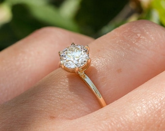 May include: A gold engagement ring with a round, clear diamond set in a six-prong setting.