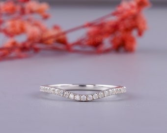 May include: A delicate, curved wedding band with a row of small, sparkling diamonds set in a silver band.