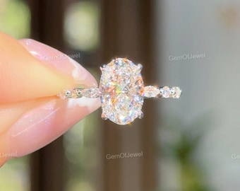 May include: A sparkling engagement ring featuring a large, oval-cut diamond as the centerpiece. The band is adorned with smaller, shimmering stones, creating a halo effect around the main diamond. The ring is set in a light-colored metal, reflecting the light.