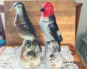 May include: Two ceramic bird decanters, one with a brown and gray bird perched on a branch and the other with a black and white bird with a red head perched on a tree stump.