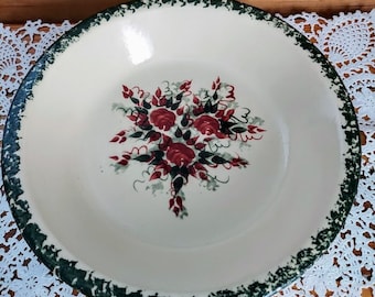 May include: A white ceramic bowl with a green rim and a floral design featuring red roses and green leaves. The bowl has a speckled green glaze.