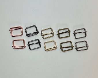 May include: A collection of ten metal rectangle sliders in various finishes, including rose gold, black, gold, and silver. These hardware pieces are designed for use in bag making, straps, or other crafting projects.
