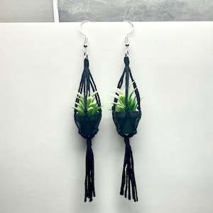 May include: A pair of black macrame earrings with a small potted plant hanging from each earring.