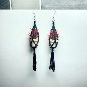 May include: A pair of black macrame earrings with small potted plants hanging from them. The plants have red leaves and are in white pots.
