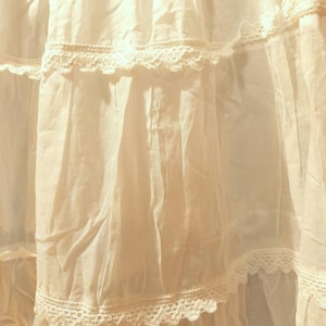 May include: Close-up of a white, layered fabric with lace detailing. The fabric is light and flowing, with visible creases and shadows. The lace trim adds a delicate touch, creating a soft, romantic aesthetic. The image suggests a garment or textile.