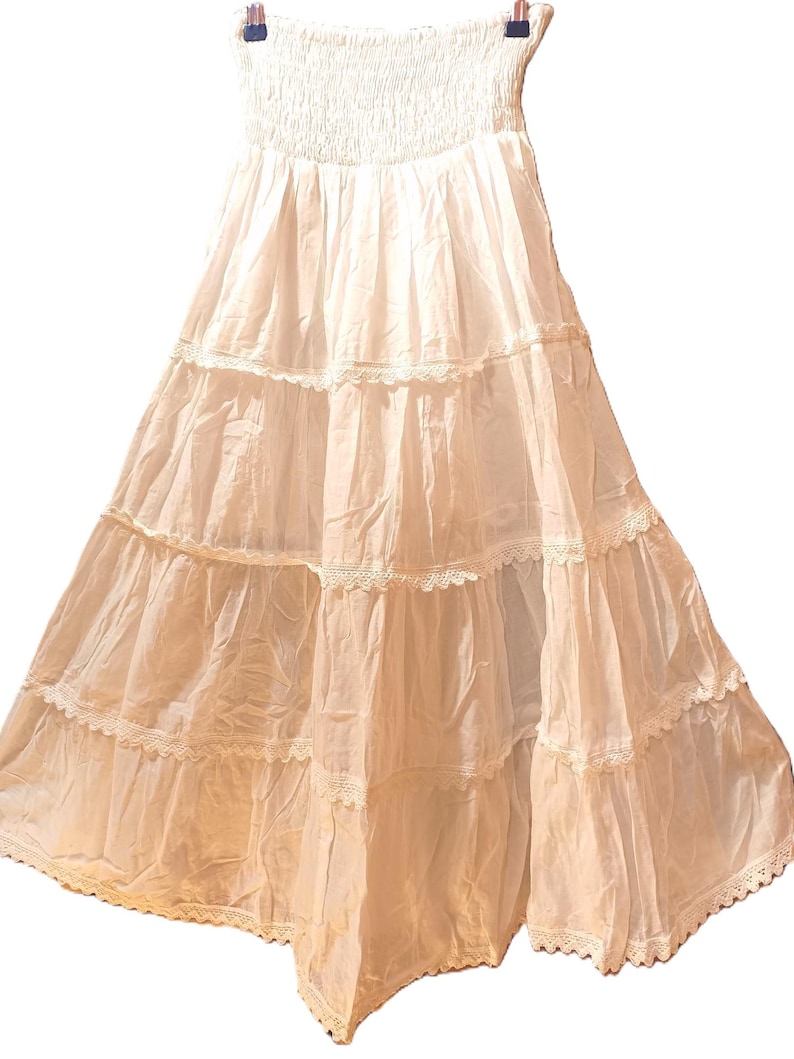 May include: A white, strapless maxi dress with a tiered skirt. The top is smocked, and each tier of the skirt is trimmed with delicate lace. The dress is made of a lightweight fabric, suitable for warmer weather.