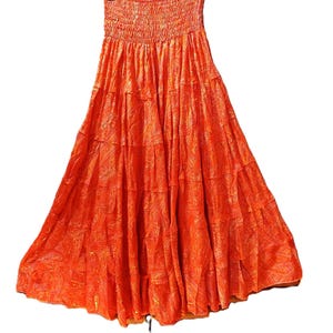 Op de afbeelding: Een feloranje maxirok met een gelaagd, vloeiend silhouet en een gesmokte elastische tailleband. De stof is over het hele oppervlak versierd met een subtiel, tonaal paisley-patroon, wat zorgt voor een gestructureerde uitstraling over het ontwerp.
