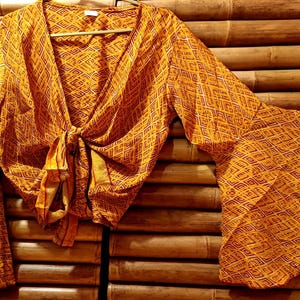 May include: A long-sleeved, orange and brown patterned blouse with a tie at the front. The blouse has a V-neck and bell sleeves.