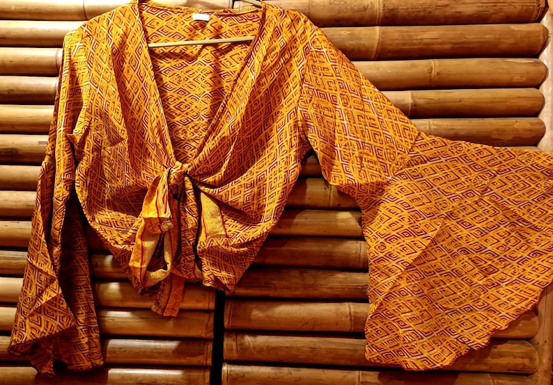 May include: A long-sleeved, orange and brown patterned blouse with a tie at the front. The blouse has a V-neck and bell sleeves.