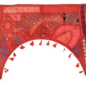 Puede incluir: Un tapiz de pared rojo en forma de arco que presenta un mosaico de diversas texturas de tela, bordados intrincados, pequeños detalles de espejos reflectantes y borlas rojas decorativas que cuelgan a lo largo del borde inferior curvo.
