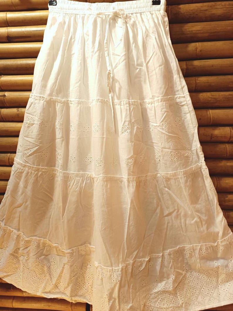 May include: A white tiered skirt with eyelet detailing and a drawstring waist. The skirt is made of a lightweight fabric and has a flowing, feminine silhouette. The skirt is approximately 36 inches long.