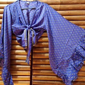 May include: A blue wrap top with a small, repeating pattern in yellow and white. The top has long, flared sleeves with ruffled cuffs and a tie closure at the waist. The fabric appears to be lightweight.