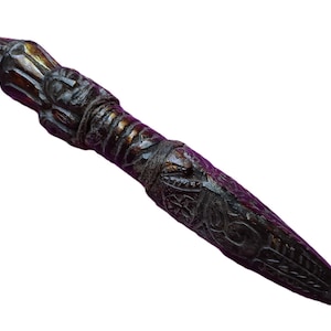 May include: A dark brown, carved wooden dagger featuring an intricate handle with a sculpted face and a blade decorated with detailed geometric and swirling patterns. The object has a polished finish with visible wood grain and dark highlights.