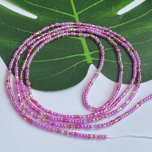 May include: A collection of pink and gold waist beads. The beads are strung together on a white string. The beads are a mix of pink, gold, and clear beads. The beads are arranged in multiple strands.