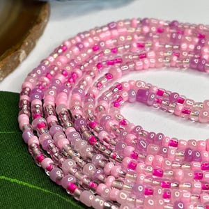May include: A multi-strand beaded necklace featuring pink, purple and clear beads. The beads are arranged in a circular pattern and have a glossy finish.