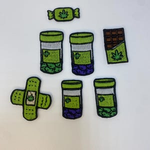 以下が含まれることがあります： 大麻をテーマにしたデザインの刺繍パッチ。パッチには、キャンディーの包み紙、チョコレートバー、ピルボトル、絆創膏が含まれており、すべて大麻の葉のモチーフが付いています。パッチは緑、紫、茶色で、白と黒のアクセントが付いています。