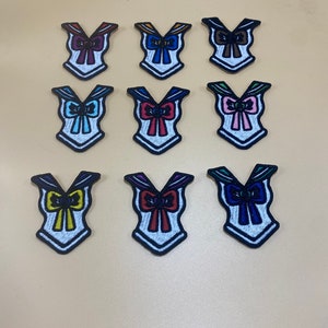May include: Ten embroidered sailor collar patches with different coloured bows. The patches are white with black outlines and feature a small black star in the centre of each bow.