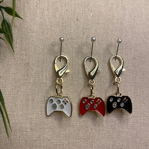 May include: Three gold-coloured keychains with a video game controller charm. The controllers are white, red, and black.