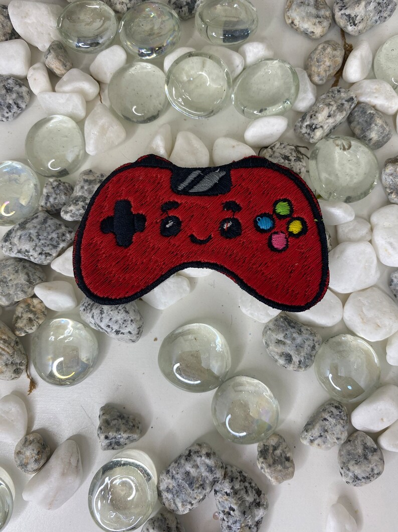Op de afbeelding: Rode geborduurde videogamecontroller-patch met een glimlachend gezicht en kleurrijke knoppen.