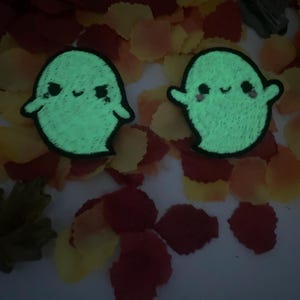 May include: Two green glow-in-the-dark ghost-shaped embroidered patches with smiling faces.
