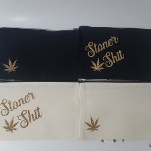 May include: Two zippered pouches with a white background and black background. Both pouches have a gold glitter marijuana leaf and the text "Stoner Shit" in gold glitter.