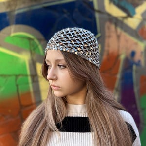 May include: A woman with long brown hair is wearing a silver sequined hat. The hat is a mesh design with small silver sequins. The woman is wearing a white and black striped sweater.