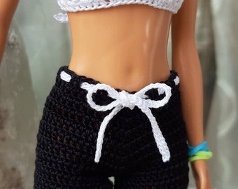 May include: A white crochet halter top and black crochet shorts with a white drawstring bow. The doll is wearing a blue and green bracelet. The outfit is handmade.