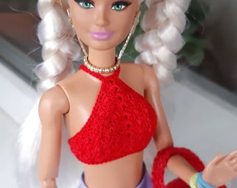 May include: A doll with blonde braided hair, wearing a red crocheted halter top, a lavender pleated skirt, and a red crocheted bag.