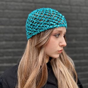 May include: A turquoise blue sequined mesh hat. The hat is made of a stretchy material and has a loose fit.
