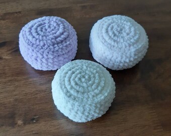 Könnte beinhalten: Drei gehäkelte runde Hocker in den Farben Lavendel, Helllila und Weiß. Die Hocker sind aus einem flauschigen Garn gefertigt und haben eine strukturierte Oberfläche.