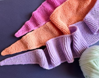 May include: Three knitted scarves in shades of pink, orange and purple. The scarves are arranged in a pile, with the purple scarf on top.
