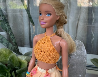 May include: A blonde doll wearing a crocheted orange halter top and a yellow skirt with pink heart-shaped accents and the text "LOL OMG" repeated on the skirt.