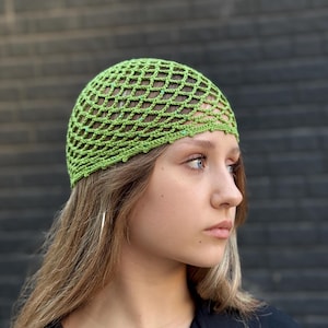 以下が含まれることがあります： ライムグリーンのネットのようなデザインの、かぎ針編みの帽子。帽子は柔らかく、質感のある糸でできており、頭に被ります。帽子はスタイリッシュなアクセサリーです。
