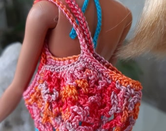 May include: A crocheted beach bag made with pink, orange and peach coloured yarn. The bag has a wide, flat base and a single strap.