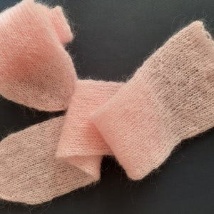 May include: A soft, pink knitted scarf made of mohair yarn. The scarf is folded and draped on a dark grey surface.
