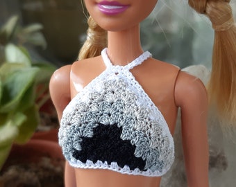 May include: A doll wearing a white crocheted halter top with a black and grey ombre design and a lavender pleated skirt.