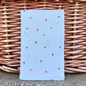 May include: A white fabric pouch with a small pink floral pattern. The pouch has a red stitched border.