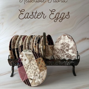 May include: A collection of reusable fabric Easter eggs in a decorative metal stand. The eggs display diverse patterns, including floral, rabbit, and toile designs. The stand has an ornate handle. Text reads "Reusable Fabric Easter Eggs".