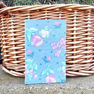 May include: A small, gray fabric pouch with a floral pattern. The pattern features pink and blue flowers, green leaves, and white dots. The pouch is sitting on a woven wicker basket.
