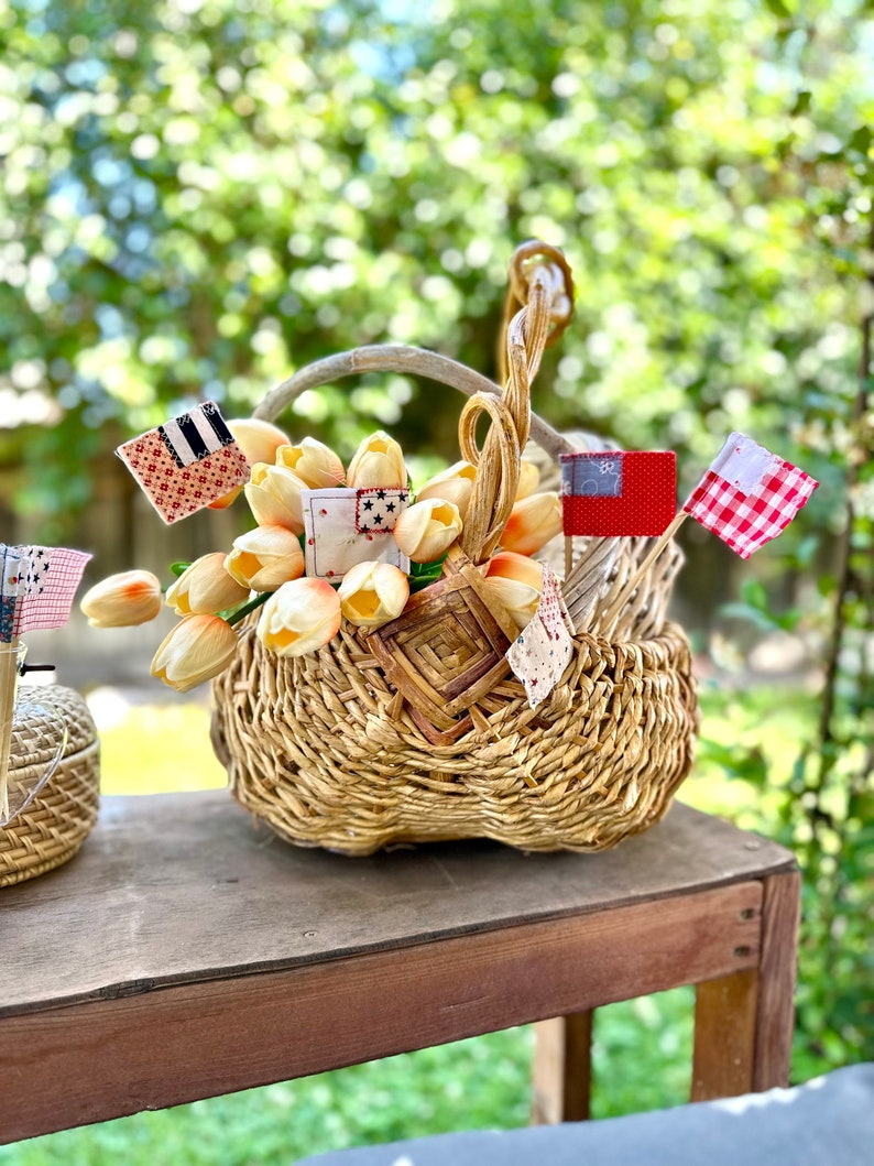 May include: A wicker basket filled with peach-colored silk flowers, decorated with small fabric flags in red, white, and blue.