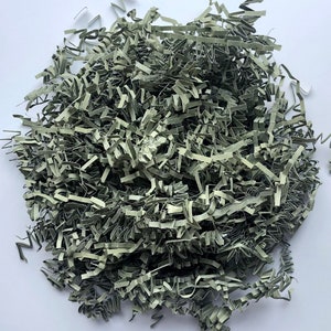 May include: A pile of shredded paper in a muted green color. The paper is cut into thin strips with a crinkled texture, creating a voluminous and textured appearance. This packaging material is ideal for cushioning and protecting items.