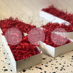 Pode incluir: Tr&ecirc;s caixas retangulares brancas preenchidas com papel picado vermelho brilhante. As caixas est&atilde;o dispostas sobre uma superf&iacute;cie salpicada. O texto "kim's little cake studio" &eacute; vis&iacute;vel nas caixas.