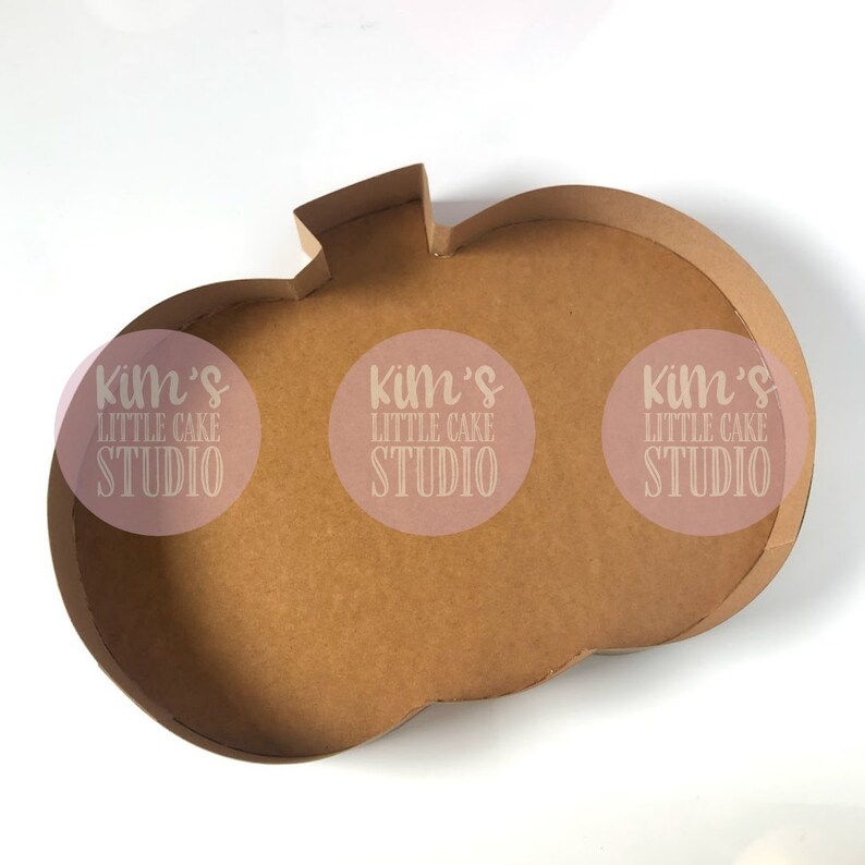 May include: A brown cardboard pumpkin-shaped box with a stem. The box has a wide, open interior and is designed for holding items. The text "kim's LITTLE CAKE STUDIO" is printed on the box.