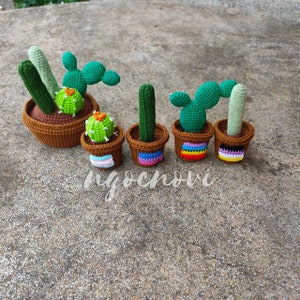 Peut inclure: Cinq cactus en crochet dans des pots bruns avec des bandes colorées autour du haut. Les cactus sont verts et ont des formes et des tailles différentes.