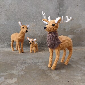 May include: Three crocheted deer figurines, one large with antlers, one medium, and one small. The deer are brown with white accents and the large deer has a brown fur collar.